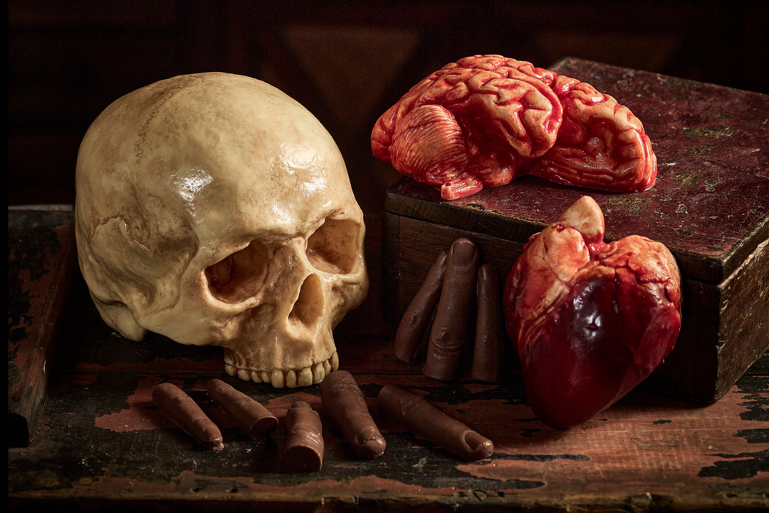 An assortment of milk and white chocolate pieces shaped and painted to represent various human anatomical structures, displayed on a wooden surface.