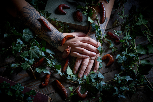 Person with tattoos holding hands over a wooden surface with chocolate garden slugs and green leaves. The edible museum chocolate realistic slugs for gifting. 