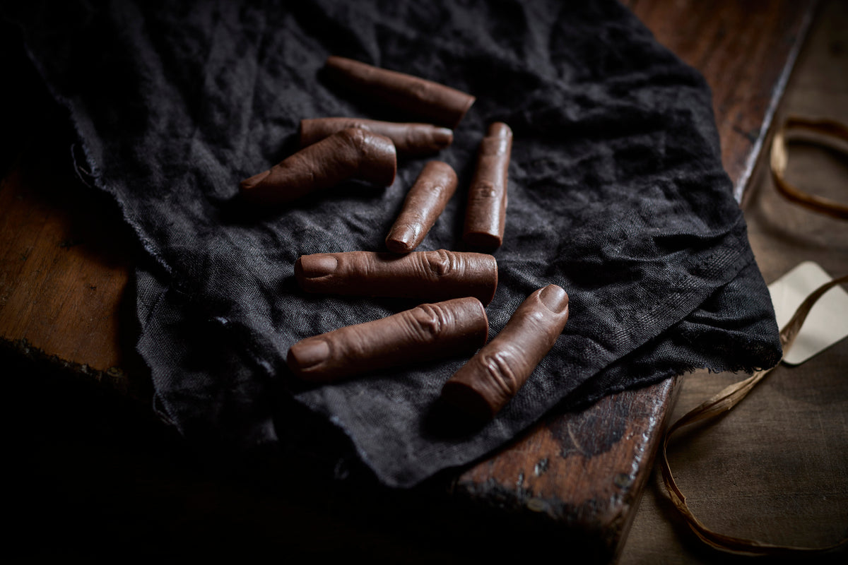 A selection of chocolate fingers arranged on a dark cloth, with varying focus on their detailed texture. Halloween Theme Gifts made from Chocolate by the Edible Museum Store 